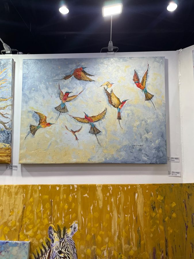 Painting of small birds in flight against a pale grey wash, hung above a gold and ochre artwork